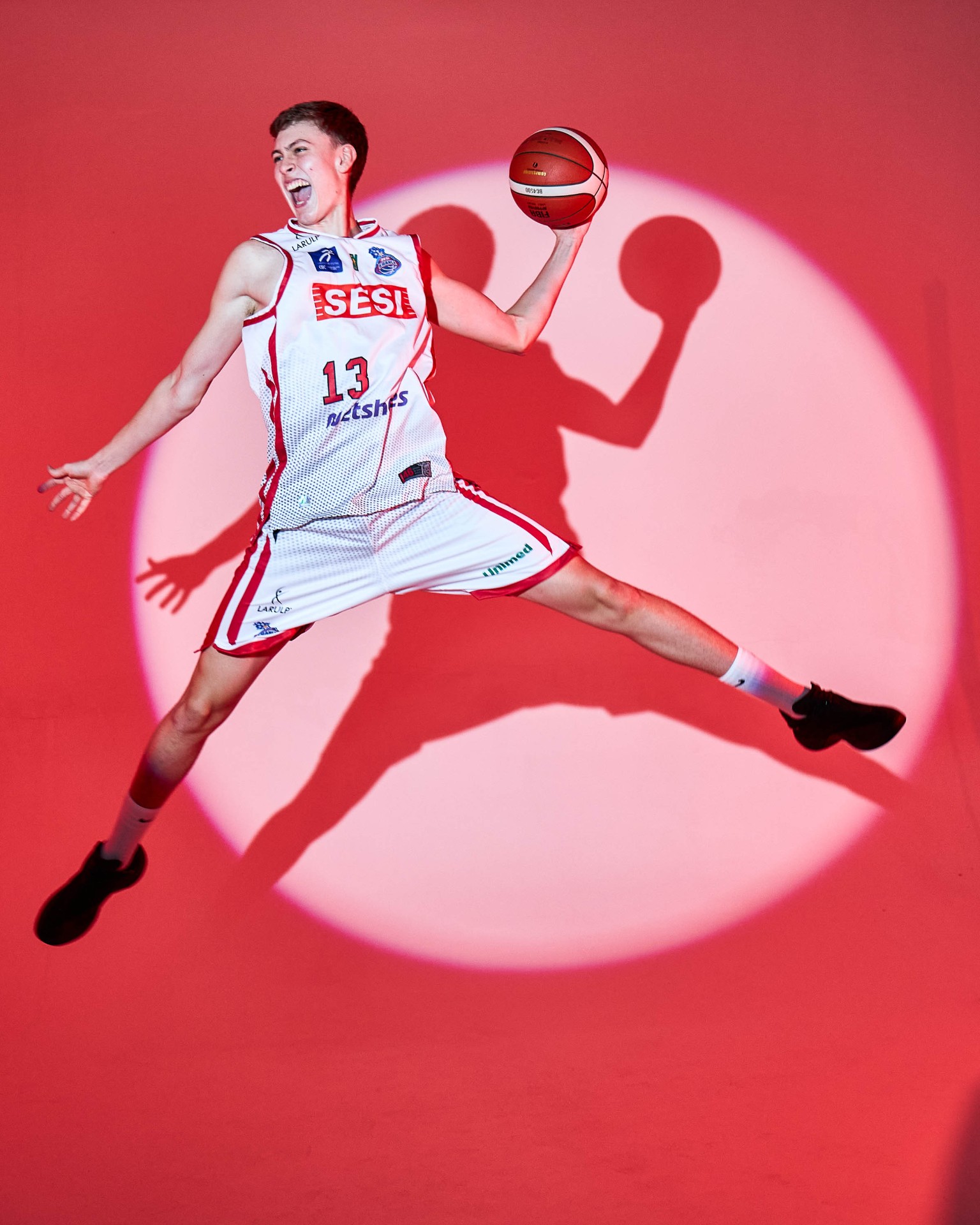 Atleta de basquete saltando com bola em fundo vermelho