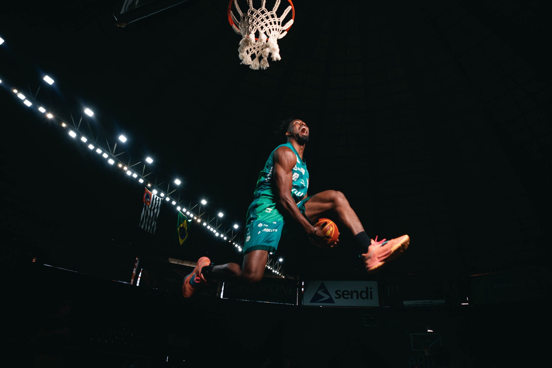 Atleta de basquete em enterrada, contra-luz na quadra